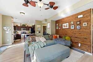 Living room with wood walls, light wood-type flooring, a ceiling fan, and an accent wall