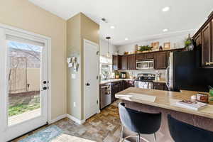 Kitchen with dark brown cabinetry, a kitchen breakfast bar, a peninsula, light countertops, and stainless steel appliances