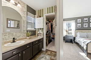 Full bathroom featuring wallpapered walls, vanity, a spacious closet, and connected bathroom