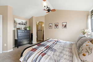 Carpeted bedroom featuring vaulted ceiling, arched walkways, and a ceiling fan