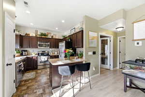Kitchen featuring dark brown cabinetry, stainless steel appliances, a kitchen bar, light countertops, and tasteful backsplash