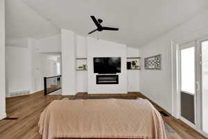 Bedroom with lofted ceiling, wood finished floors, a glass covered fireplace, and ceiling fan