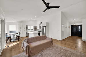 Living area with lofted ceiling, healthy amount of natural light, light wood-style floors, and a ceiling fan