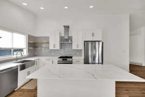Kitchen with stainless steel appliances, light stone counters, white cabinets, wall chimney range hood, and recessed lighting