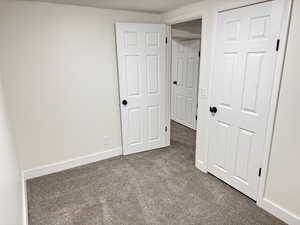 Unfurnished bedroom with dark carpet and baseboards
