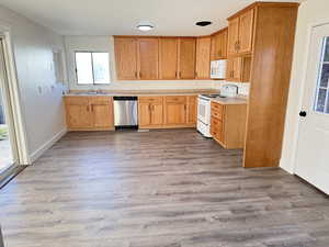 Kitchen with light countertops, white appliances, light wood-type flooring, and brown cabinetry