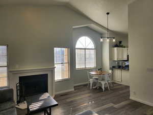 Dining area with dark wood finished floors, vaulted ceiling, and a fireplace with flush hearth