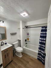 Full bathroom with vanity, a textured ceiling, dark wood-style flooring, and shower / tub combo with curtain