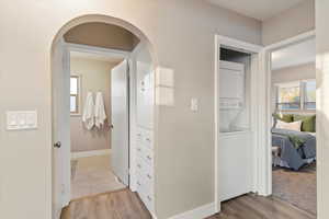 Hall featuring light wood finished floors, stacked washing machine and dryer, and arched walkways