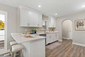 Kitchen featuring arched walkways, white cabinetry, a peninsula, a breakfast bar, and light stone countertops
