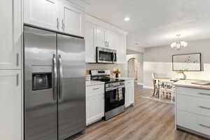 Kitchen with appliances with stainless steel finishes, white cabinets, arched walkways, light wood-style floors, and recessed lighting