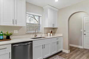 Kitchen with stainless steel dishwasher, white cabinets, light stone counters, and light wood-style flooring