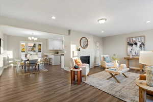 Living area with a brick fireplace, a chandelier, dark wood-style flooring, and recessed lighting