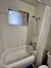 Bathroom featuring toilet and shower / bath combination with curtain