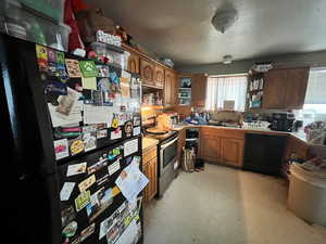 Kitchen with black appliances, light flooring, brown cabinets, and light countertops