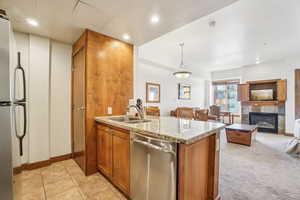 Kitchen with light stone counters, stainless steel appliances, a peninsula, brown cabinetry, and decorative light fixtures
