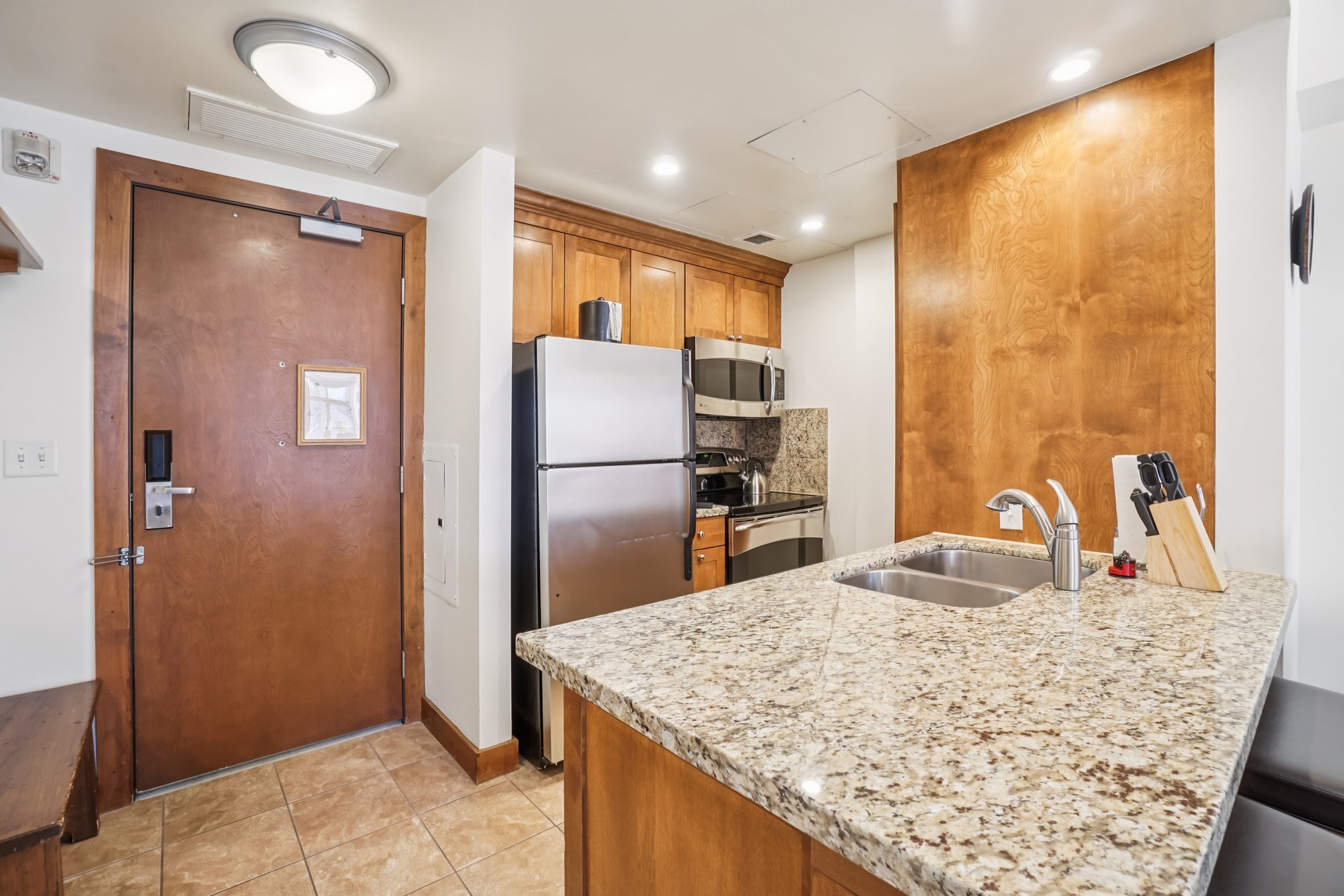 Kitchen featuring brown cabinetry, appliances with stainless steel finishes, a peninsula, light stone counters, and light tile patterned flooring