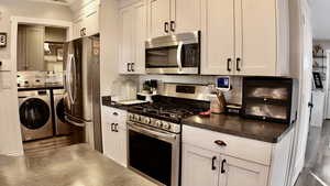 Kitchen featuring separate washer and dryer, appliances with stainless steel finishes, LVP finished floors, dark countertops, and white cabinets