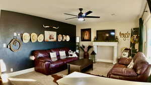 Carpeted living room featuring an accent wall, and a ceiling fan.