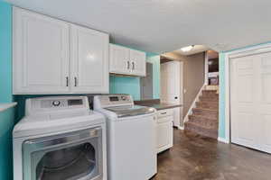 Laundry room with concrete flooring, a textured ceiling, cabinet space, and washer and clothes dryer