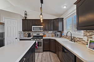 Kitchen with vaulted ceiling, appliances with stainless steel finishes, dark brown cabinets, pendant lighting, and light countertops
