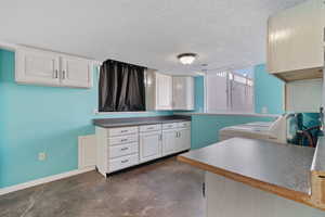 Kitchen featuring finished concrete floors, a textured ceiling, white cabinetry, washer / dryer, and dark countertops