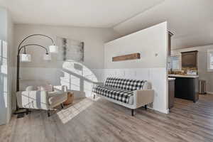 Living area featuring lofted ceiling, light wood-style flooring, and a wainscoted wall
