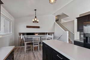 Kitchen with dark cabinetry, light wood-style flooring, stainless steel fridge, hanging light fixtures, and vaulted ceiling