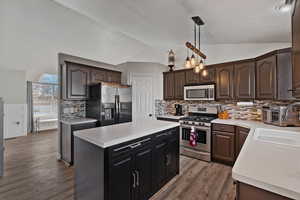 Kitchen featuring stainless steel appliances, light countertops, hanging light fixtures, a kitchen island, and lofted ceiling