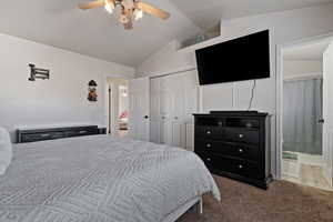 Carpeted bedroom featuring vaulted ceiling, ensuite bath, a closet, and ceiling fan
