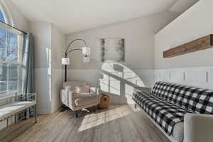 Living room featuring wainscoting, vaulted ceiling, and wood finished floors