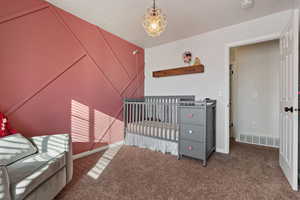 Bedroom with a nursery area, carpet flooring, a chandelier, and a textured ceiling