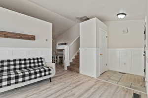 Entrance foyer featuring a wainscoted wall, a decorative wall, lofted ceiling, light wood finished floors, and stairway
