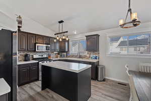 Kitchen featuring a chandelier, vaulted ceiling, appliances with stainless steel finishes, a center island, and decorative light fixtures