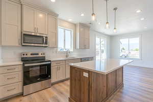 Kitchen with stainless steel appliances, light wood-style floors, hanging light fixtures, a kitchen island, and recessed lighting