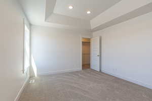 Unfurnished bedroom with a tray ceiling, a walk in closet, carpet floors, and recessed lighting