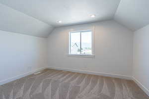 Additional living space featuring a textured ceiling, vaulted ceiling, and light carpet