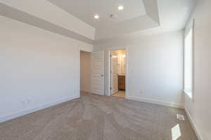 Unfurnished bedroom with a tray ceiling, light carpet, and ensuite bathroom