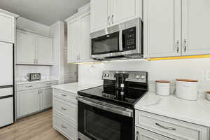 Kitchen with stainless steel appliances, light wood finished floors, light stone countertops, and white cabinets