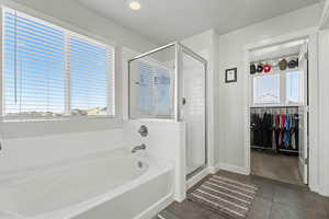 Full bathroom with a spacious closet, a garden tub, a shower stall, and dark tile patterned floors
