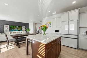 Kitchen with freestanding refrigerator, a center island, light wood-style floors, white cabinetry, and recessed lighting