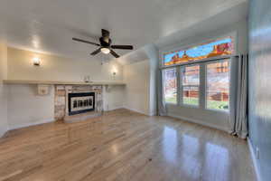 Unfurnished living room featuring oak floors, a stone fireplace, ceiling fan, and vaulted ceiling