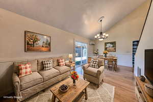 Living room featuring a wainscoted wall, beautiful oak floors, high vaulted ceiling, and a chandelier