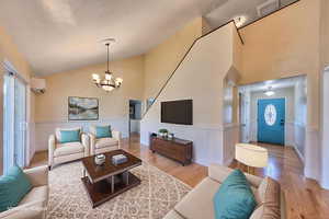 Living room featuring wainscoting, hardwood oak floors, a chandelier, high vaulted ceiling, and a wall unit AC