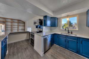 Kitchen with stainless steel appliances, blue cabinetry, light  granite countertops, plenty of natural light, and lofted ceiling