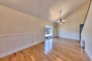 Dining area with lofted ceiling, wainscoting, light oak floors, and chandelier