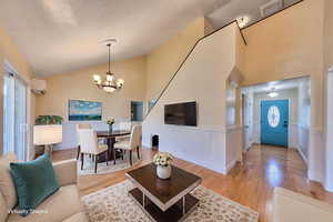 Living area with wainscoting, light oak flooring, a chandelier, high vaulted ceiling, and an AC wall unit