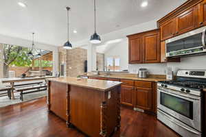 Kitchen with appliances with stainless steel finishes, hanging light fixtures, dark wood finished floors, a center island, and a textured ceiling