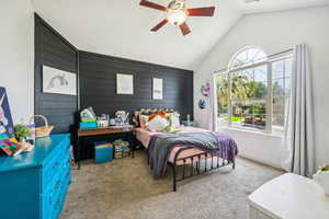 Bedroom featuring carpet flooring, wooden walls, an accent wall, lofted ceiling, and a ceiling fan