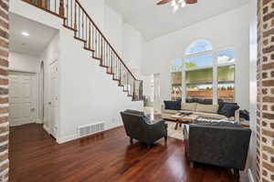 Living room featuring high vaulted ceiling, dark wood-type flooring, brick wall, arched walkways, and stairs